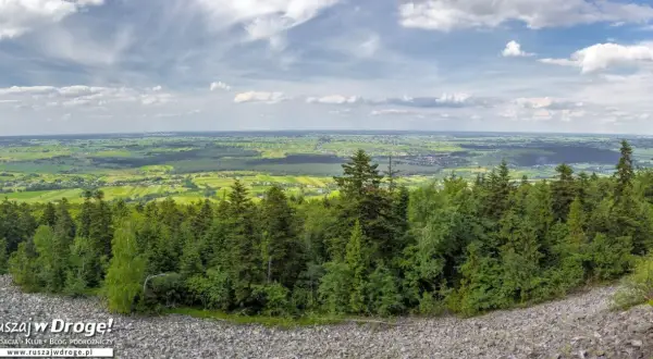Widok z góry na zielone pola i lasy, idealne na fajne miejsca w świętokrzyskim na weekend. Kamieniste zbocze i chmury na niebie.