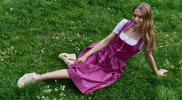 Junge Frau im Dirndl sitzt auf einer grünen Wiese mit Gänseblümchen.