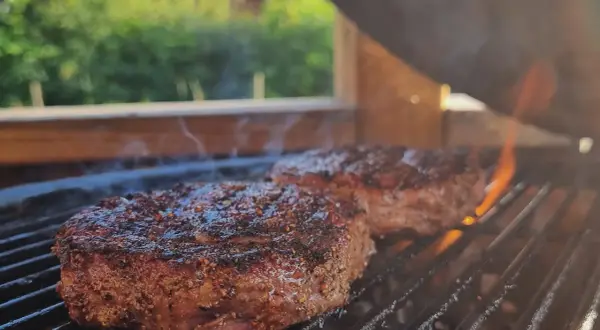 Två saftiga biffar med kryddor grillas över glödande kol. Perfekt för en sommarfest, undrar vad man kan grilla mer?