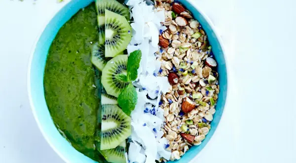 En grön, nyttig smoothie bowl med kiwi, kokosflingor och granola.