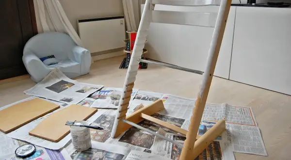 Måla om Stokke stol med vit färg. Trädelar och pensel ligger på tidningspapper.