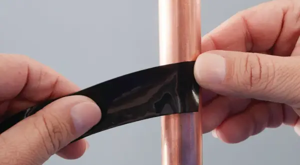Hände dichten mit schwarzem Klebeband ein kleines Loch in einer Kupferwasserleitung ab.