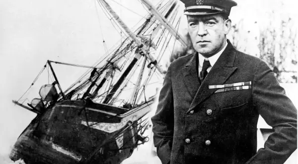 Ernest Shackleton, en modig polarforskare, står framför sitt skepp som fastnat i isen.