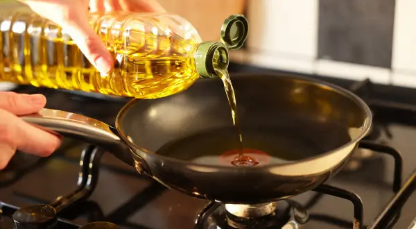 Mano versa olio in padella sul fornello, pronto per friggere.