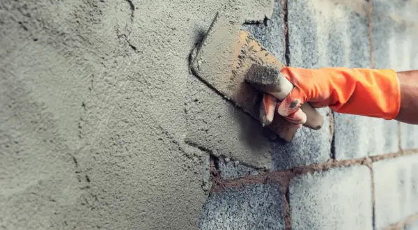 Mano con guanto arancione stende malta per stuccare muri in pietra con una cazzuola.