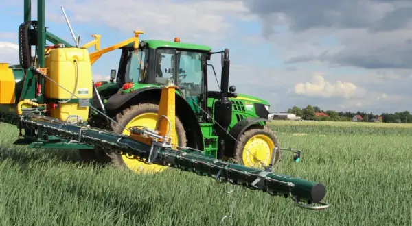 Zielony traktor z opryskiwaczem na polu. Warto sprawdzić movento 100 sc dawkowanie dla optymalnych rezultatów.