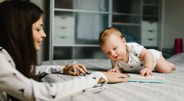 Kobieta czyta książkę dziecku leżącemu na łóżku.