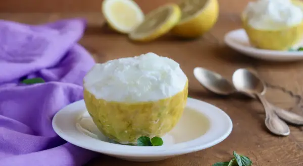 Sorbetto al limone senza albume servito in un limone scavato, con limoni affettati e un tovagliolo viola sullo sfondo.