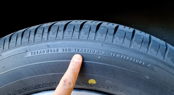 Palec wskazuje na oznaczenie "TREADWEAR 260 TRACTION A TEMPERATURE A" na oponie, informujące o jej właściwościach i dacie produkcji.
