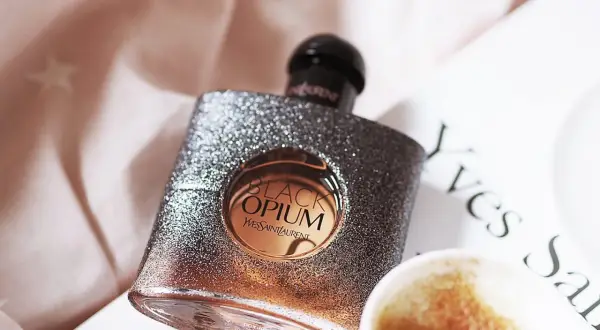 Błyszcząca butelka Black Opium od YSL, z nutą **opium floral shock**, obok filiżanki kawy i książki.