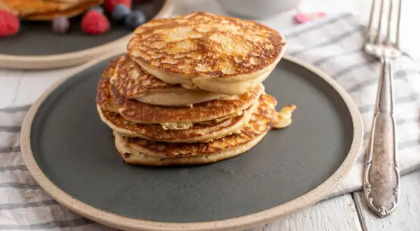 Stos puszystych fit pancakes z odżywki białkowej, ozdobiony malinami i borówkami, czeka na widelcu.