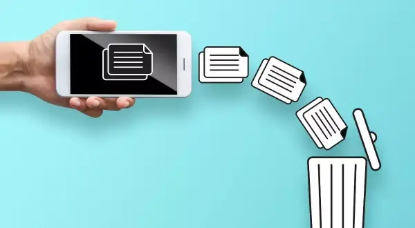 Dłoń trzyma smartfon, z którego wypadają dokumenty prosto do kosza. Tak właśnie działa opcja "gdzie jest kosz w telefonie" przy usuwaniu plików.