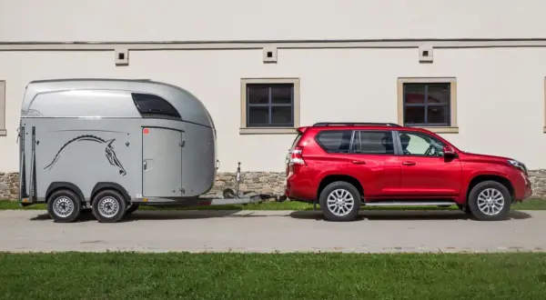 Czerwony SUV ciągnie przyczepę z koniem.