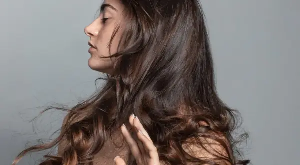 Mujer con ojos cerrados y pelo bonito, moviéndose con el viento.