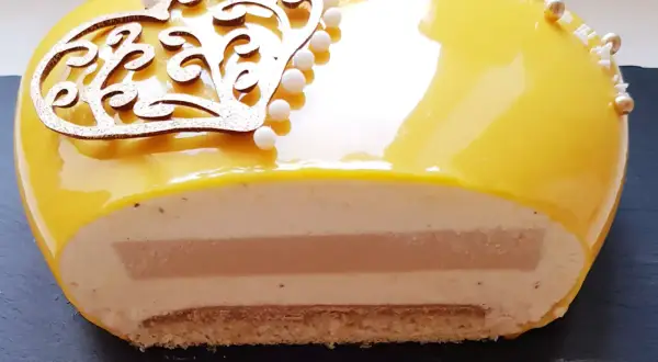 Entremet cœur jaune vif, décoré d'une arabesque dorée et de perles. La coupe révèle des couches onctueuses et un insert caramel beurre salé.