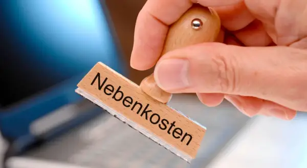 Stempel mit "Nebenkosten" wird über Laptop gehalten. Was darf nicht rein? Klare Regeln für die Nebenkostenabrechnung sind wichtig.