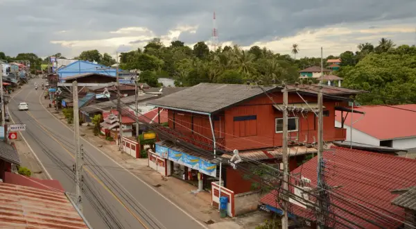 Un pueblo en el Mae Hong Son Loop, con casas rojas y azules a lo largo de una carretera, rodeado de exuberante vegetación y un cielo nublado.