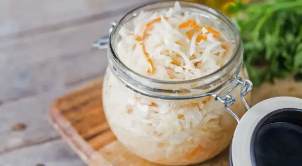Glas mit Sauerkraut, bereit zum Kohl fermentieren. Frische Kräuter im Hintergrund.