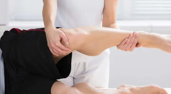 Fizjoterapeuta pomaga pacjentowi z bólem kolca biodrowego, wykonując delikatne ruchy nogą.