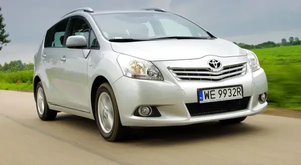 Srebrna Toyota Verso jedzie po drodze, otoczona zielonymi polami.