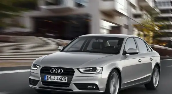 Srebrne Audi A4 B8 pędzi ulicą, rozmywając tło nowoczesnych budynków.
