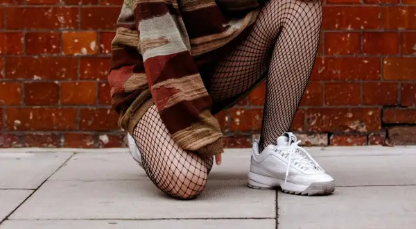 Osoba w swetrze w pasy i białych sneakersach, prezentująca, co to kabaretki – czarne, siateczkowe rajstopy.