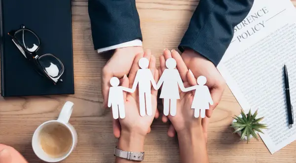 Dłonie trzymające papierową rodzinę na tle dokumentu "Insurance Policy".