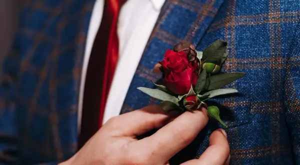 Elegancki, niebieski garnitur w kratę z czerwonym krawatem i subtelnym kwiat w butonierce.