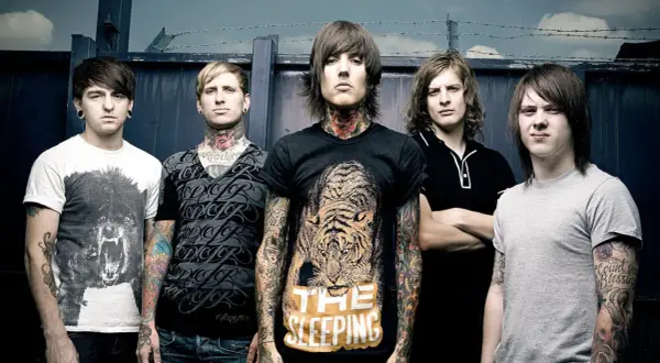 Bring Me The Horizon członkowie, z tatuażami i kolczykami, pozują przed ciemnym tłem.