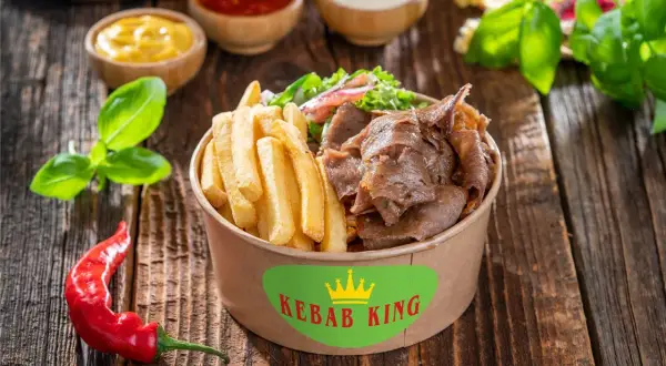 Kebab z frytkami i warzywami w pudełku Kebab King, obok sosów i papryczki chili.