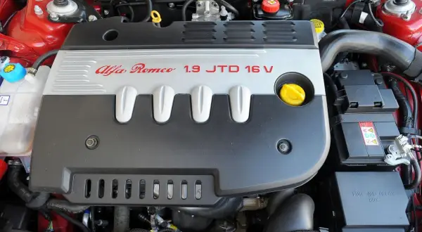 Silnik Alfa Romeo 147 1.9 JTD 16V, widok z góry. Czerwona karoseria, czarna osłona silnika z napisem.