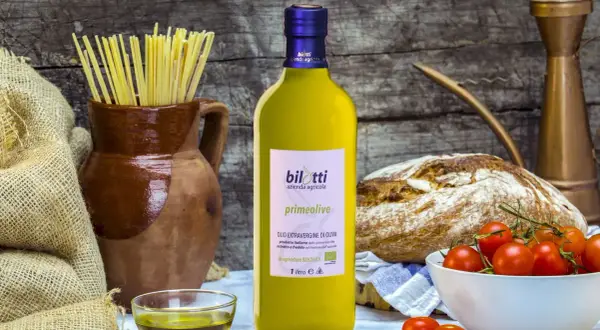 Bottiglia di olio extravergine d'oliva Bilotti, con pasta, pane, pomodorini e una ciotolina di olio, per gustare i migliori tipi di olio.