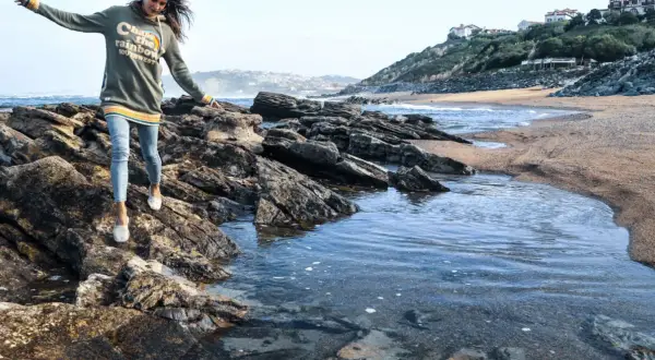 Une jeune femme profite d'une randonnée bord de mer, naviguant sur des rochers près de l'eau.