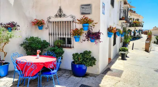 Mesa y sillas azules junto a pared blanca adornada con macetas. Un rincón encantador para descubrir qué ver en Mijas.