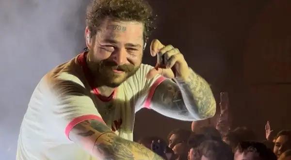 Post Malone na koncercie, uśmiecha się i pokazuje gest ręką.