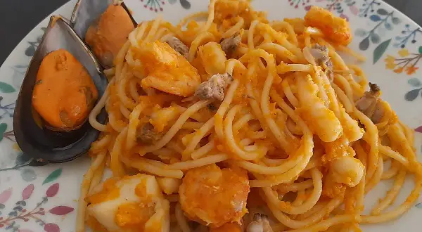 Espaguetis a la marinera con mejillones, gambas y calamares, servidos en un plato con un delicado estampado floral.