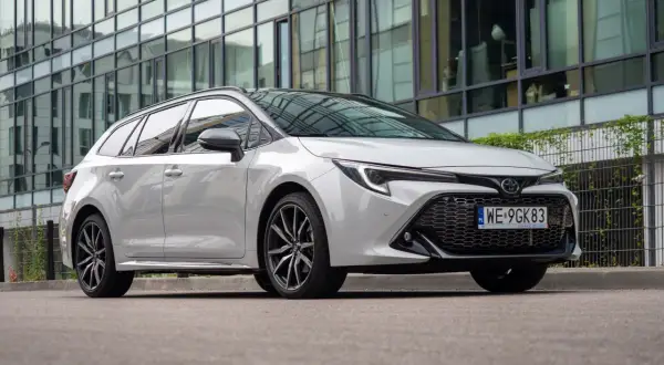 Biała Toyota Corolla 2.0 Hybrid na tle nowoczesnego budynku.