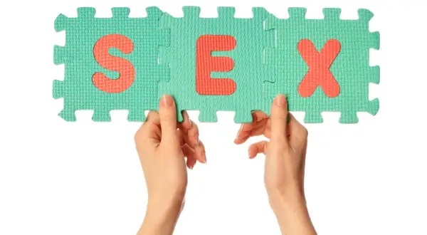 Dłonie trzymające puzzle z literami S, E, X. Symbolizuje to edukację w zakresie rozwoju seksualnego dzieci.