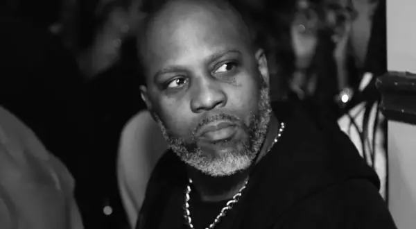 DMX, z siwą brodą i łańcuchem na szyi, spogląda w bok. W tle widać niewyraźne sylwetki, być może jego dzieci.