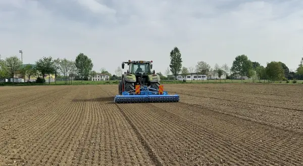 Trattore verde in azione per l'erpicatura del terreno, preparando il campo per la semina.