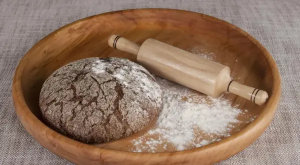 Drewniana miska z bochenkiem chleba, wałkiem i mąką. Czy pszenica durum ma gluten? Tak, zawiera go.