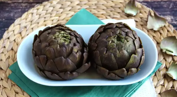 Deux artichauts violets sur une assiette blanche, prêts pour une recette d'artichaut savoureuse.