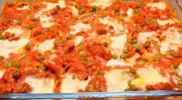 Nidi di tagliatelle al forno con ragù, piselli e mozzarella filante, un piatto invitante e saporito.