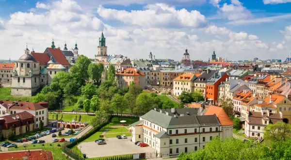 Widok na zabytkowe centrum Lublina, z charakterystycznymi kamienicami i wieżami kościelnymi, otoczone zielenią. Lubelszczyzna w pełnej krasie.