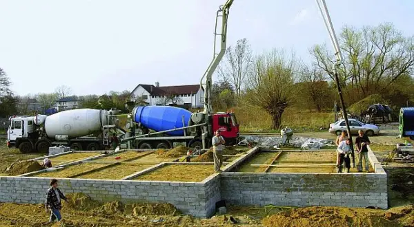 Betonowanie ławy fundamentowej. Dwie betoniarki i pompa do betonu pracują na budowie.