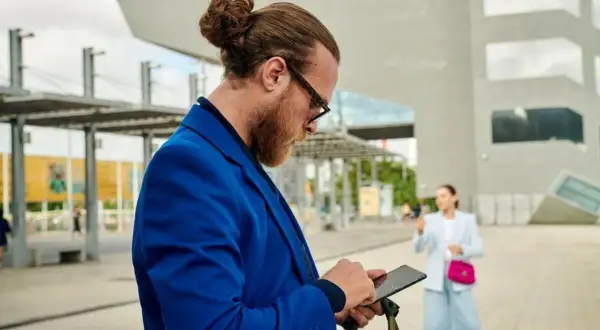Mężczyzna w niebieskiej marynarce sprawdza telefon, szukając sposobu, jak sprawdzić stan konta bez logowania.