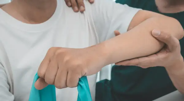 Therapeut unterstützt bei Übungen für die liebscher und bracht schulter. Ein blaues Theraband wird genutzt.