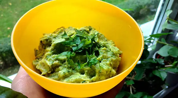Pyszne guacamole co to? Zielona pasta z awokado, doprawiona świeżą kolendrą, w żółtej miseczce.