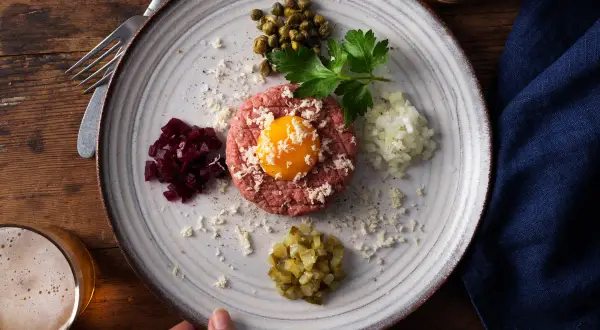 En tallrik med råbiff, äggula, kapris, hackad lök, rödbetor och gurka. Perfekt för ett klassiskt råbiff recept.