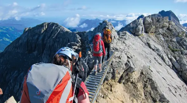 Drei Wanderer auf einer Hängebrücke während einer 5-tägigen Alpenwanderung. Die Aussicht ist atemberaubend.
